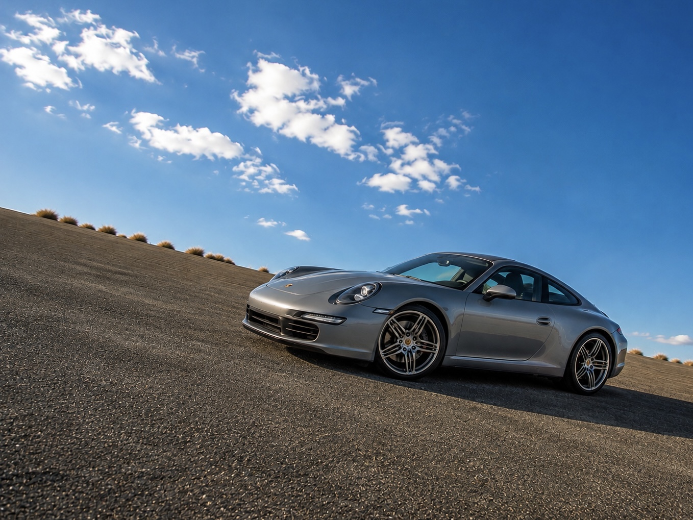Silbergrauer Porsche 911 Carrera auf einer Rennstrecke unter blauem Himmel